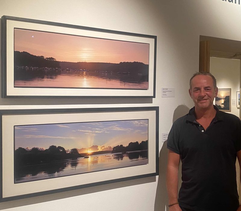 Marine artist Jamie Medlin beside his framed sunset estuary painting
