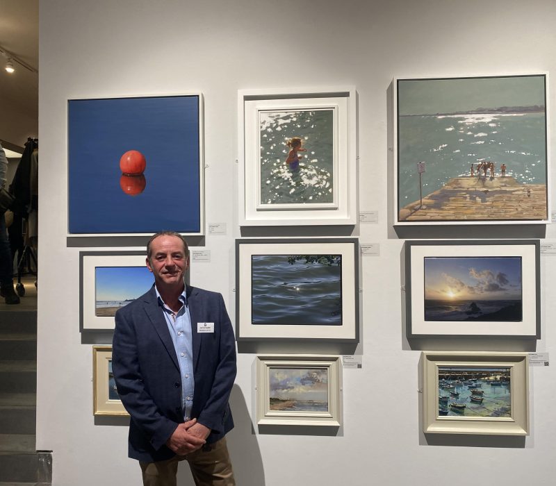 Visitor beside framed Jamie Medlin seascape paintings at an exhibition